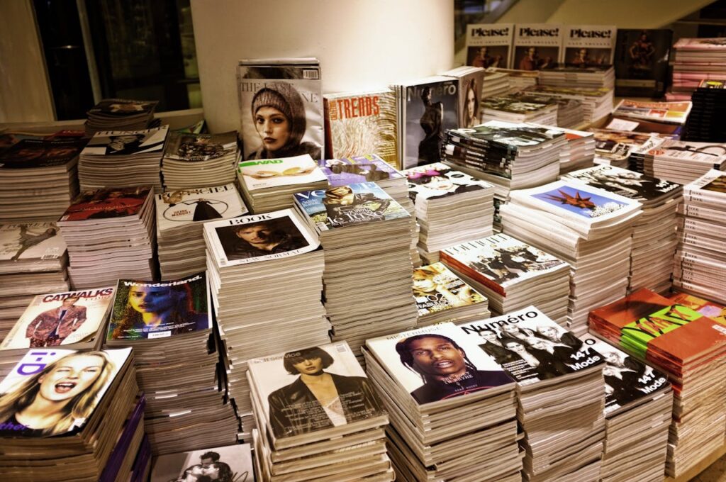 pexels-photo-264600 Huge stacks of diverse fashion and lifestyle magazines piled high in an indoor store setting.